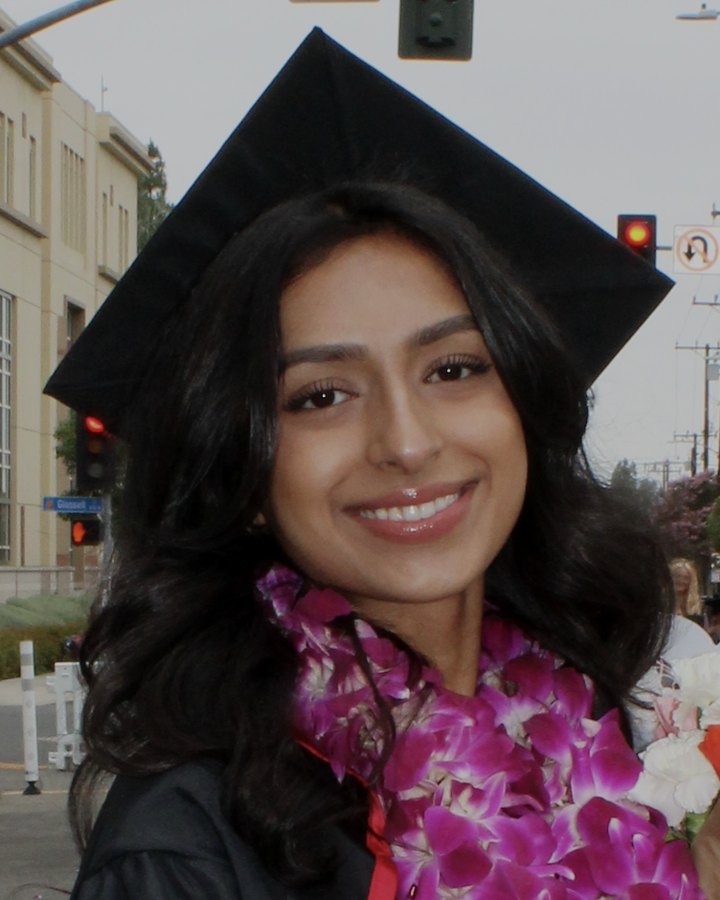 Navya at her college graduation, smiling in a cap and gown with a purple orchid lei